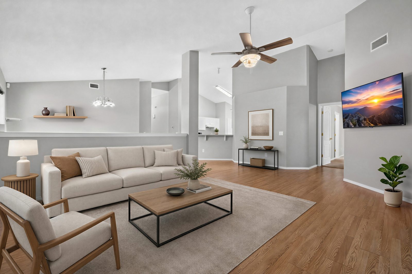 Family room, virtually staged: vaulted ceiling, ceiling fan, and wood-look laminate floor, open over a half wall to the dining room and kitchen, shown with digitally added furniture