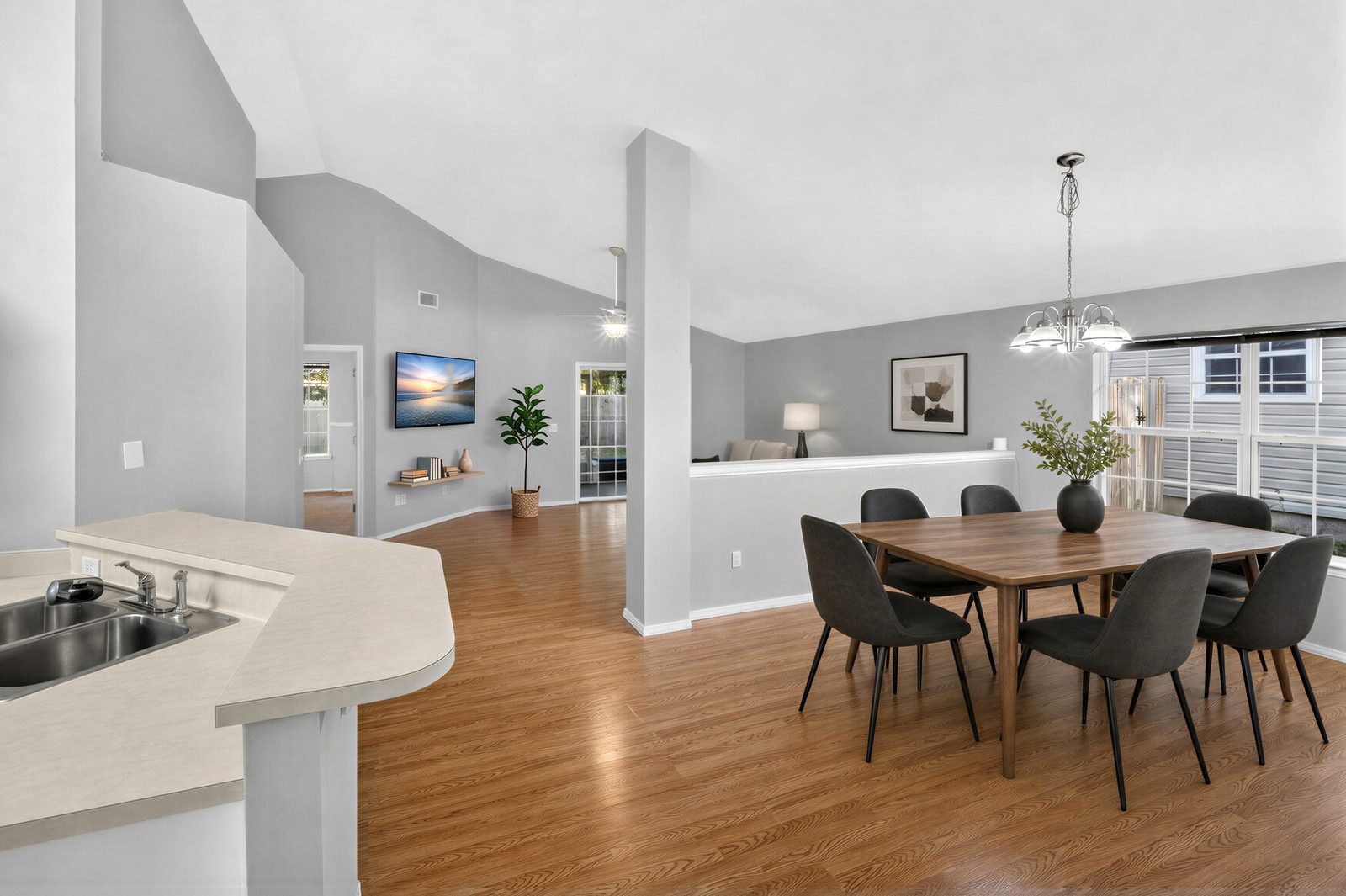View from the kitchen peninsula, virtually staged: dining room under a vaulted ceiling, open to the family room, shown with digitally added furniture