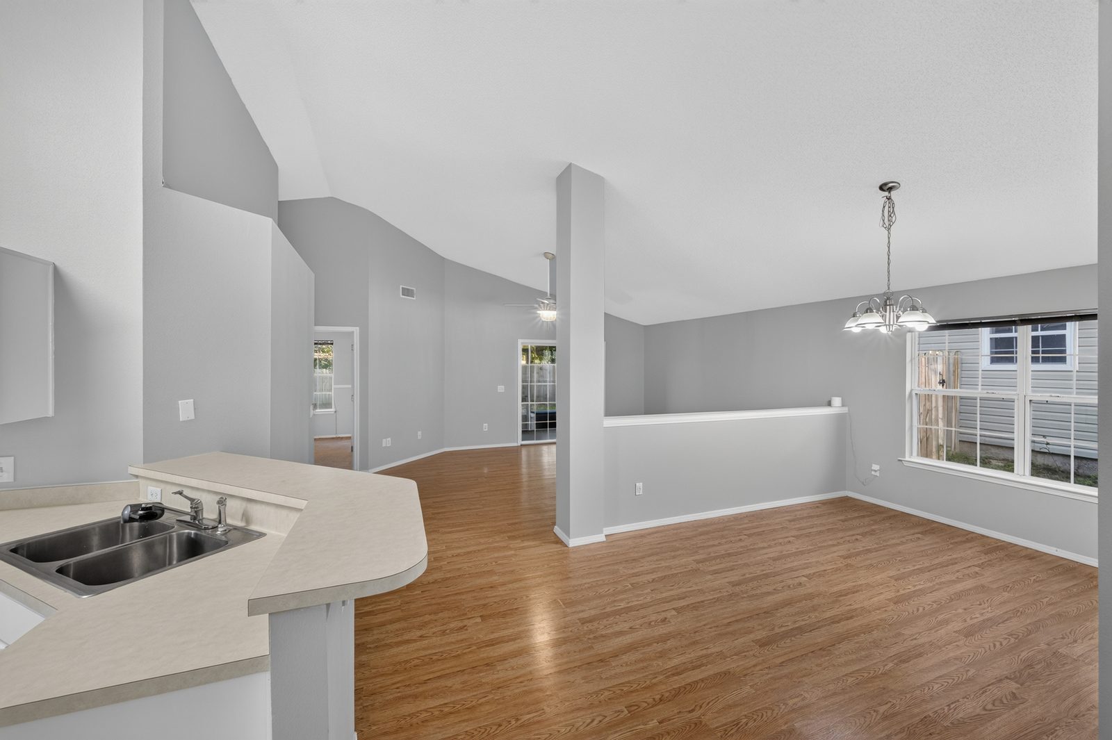 The same view empty: kitchen peninsula, dining room with a chandelier and wide window, and the family room beyond under a vaulted ceiling