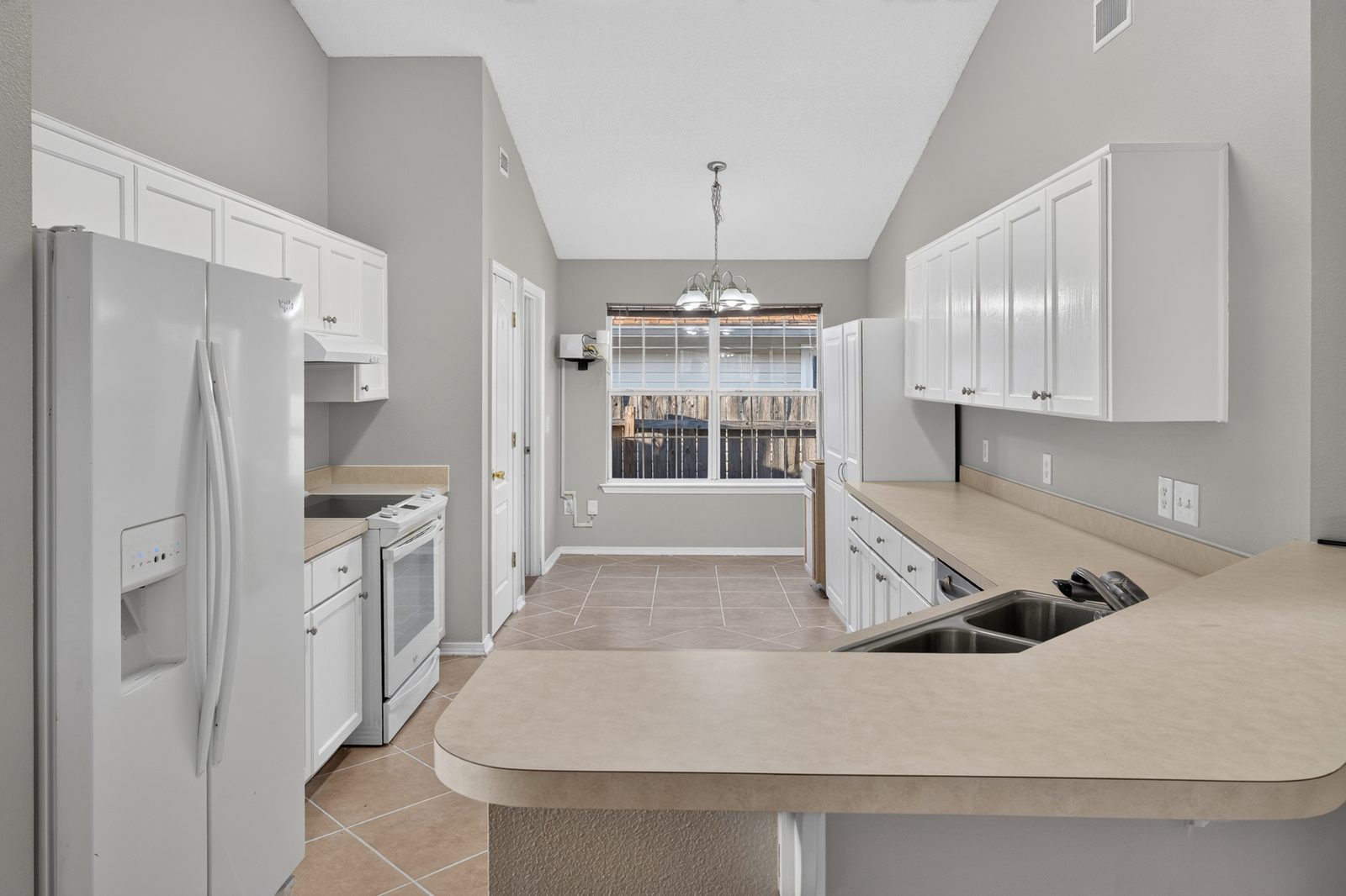 Kitchen with white cabinets, white appliances, a laminate peninsula, and the eat-in area at a wide window