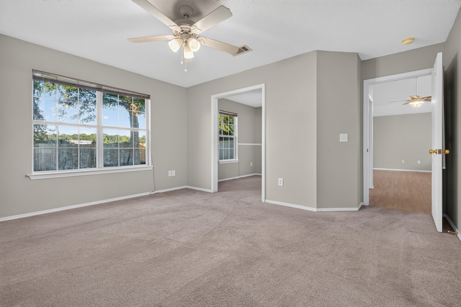 Primary bedroom with carpet, a ceiling fan, and a large window, with the office doorway on the left