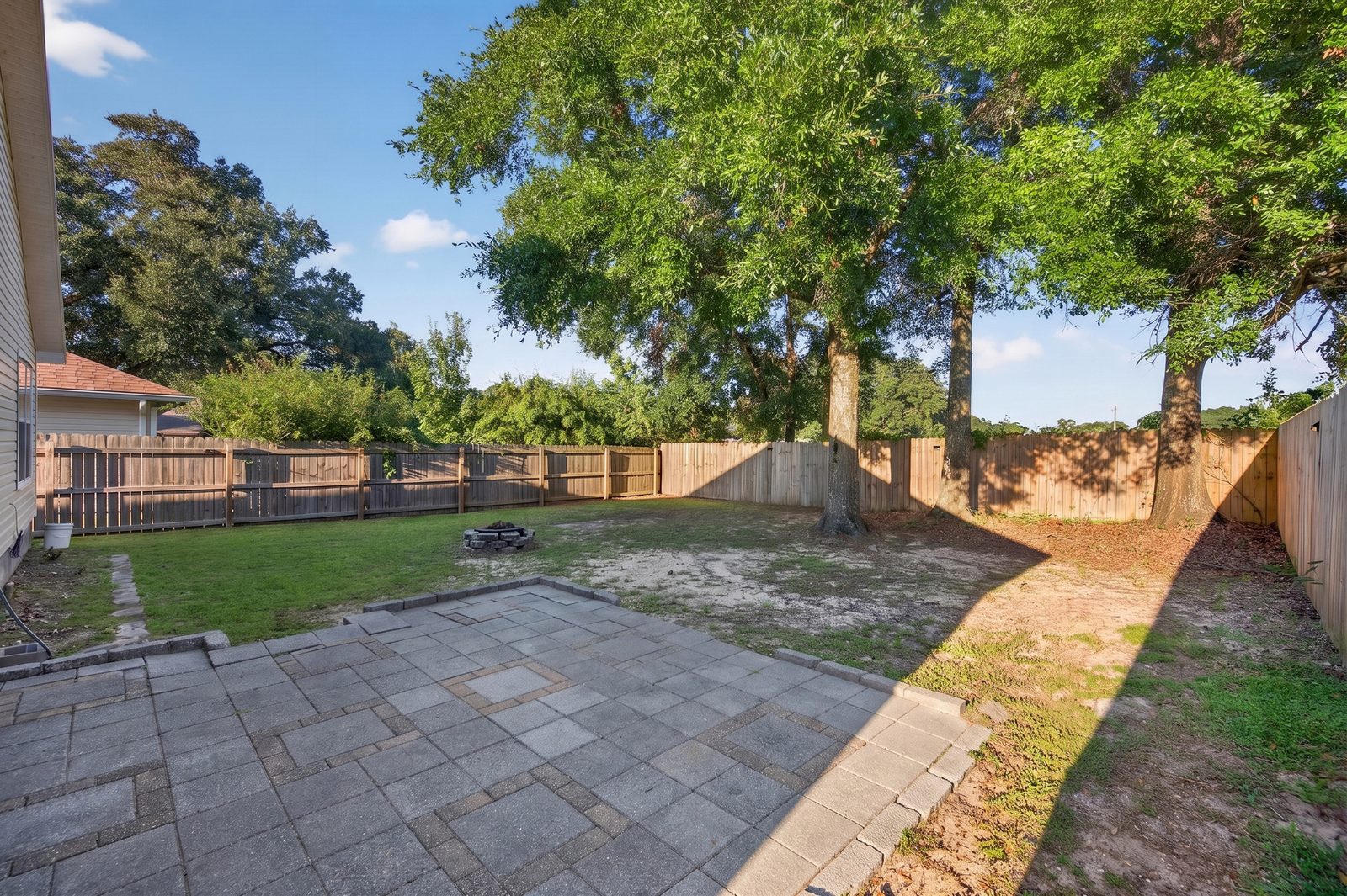 Paver patio outside the screened porch, with the fenced backyard and mature shade trees beyond
